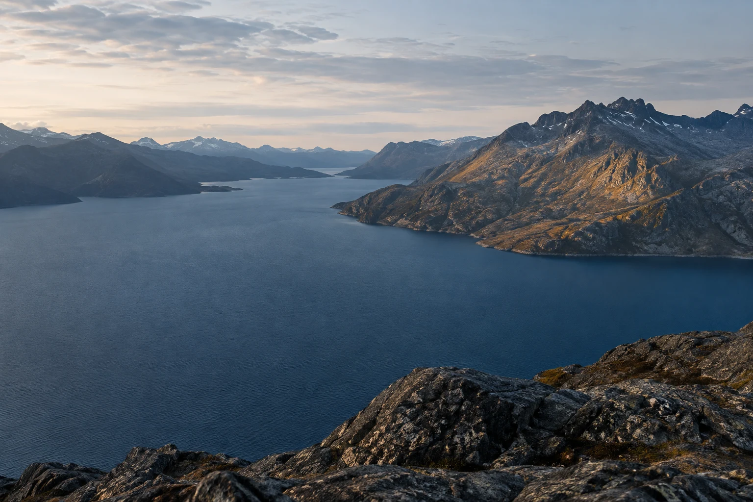 Een uitgestrekt diepblauw bergmeer, omringd door een brede bergketen.